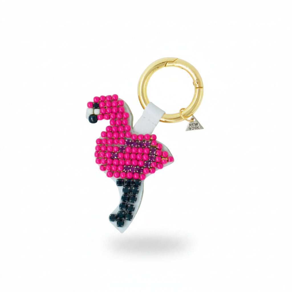 Beaded flamingo keychain attached to a cream-colored handbag on a marble surface.