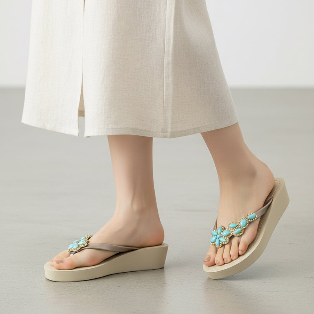 Beige sandals with turquoise embellishments worn by a person in light-colored pants on a neutral background